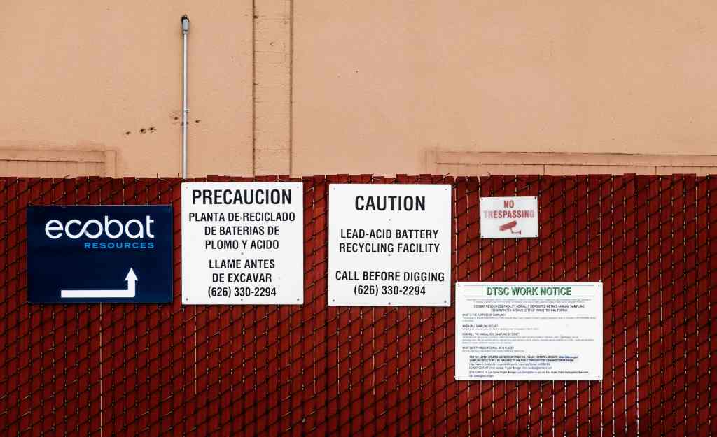 A DTSC work notice for annual sampling along the property’s perimeter is posted on the outside fence of the Ecobat facility next to cautionary signage.